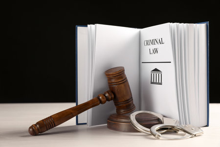 Judge's gavel, handcuffs and Criminal law book on white table against black background