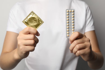 Young woman holding birth control pills and condom, closeup. safe sex conceptの写真素材