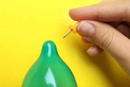 Woman piercing inflated condom with pin on yellow background, closeup. safe sexの写真素材