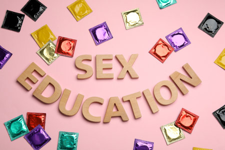 Flat lay composition with condoms and words SEX EDUCATION made with wooden letters on pink backgroundの写真素材