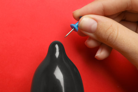Woman piercing inflated condom with pin on red background, closeup. safe sexの写真素材