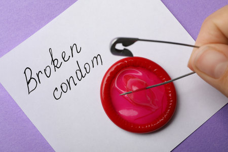 Woman piercing condom with pin on purple background, closeup. safe sexの写真素材