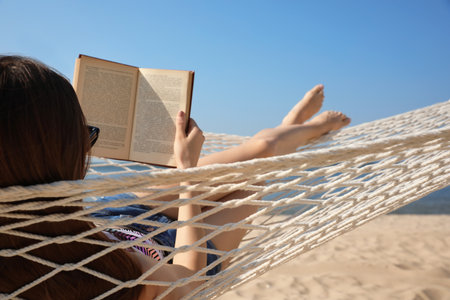 Young woman reading book in hammock on beachの写真素材