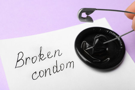 Woman piercing condom with pin on violet background, closeup. safe sexの写真素材