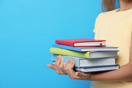 Little girl holding books on blue background, closeup. Reading conceptの写真素材
