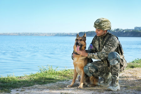 Man in military uniform with German shepherd dog near river, space for textの写真素材