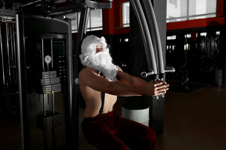 Young shirtless Santa Claus training in modern gym
