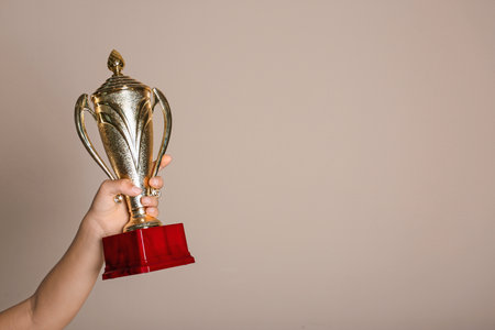 Child holding golden winning cup on beige background, closeup. Space for textの写真素材