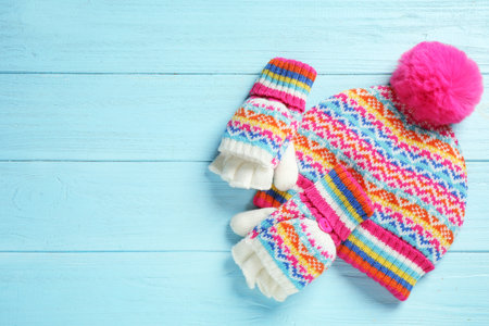 Warm knitted hat and mittens on blue wooden background, flat lay. Space for textの写真素材