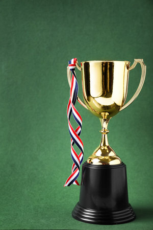 Golden trophy cup with ribbon on green backgroundの写真素材