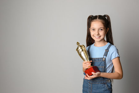 Happy girl with golden winning cup on light background. Space for textの写真素材