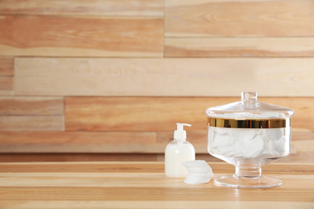 Decorative glass jar with cotton pads and cosmetic product on table against wooden background. Space for textの写真素材