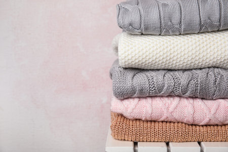Stack of knitted clothes on white wooden table against pink background, space for text. Cozy autumnの写真素材