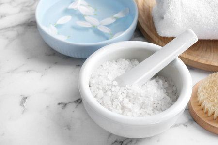 Mortar and pestle with white sea salt for spa scrubbing procedure on marble tableの写真素材