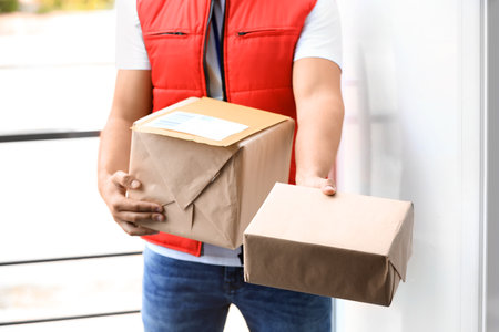 Young courier delivering parcels on doorstep, closeupの写真素材