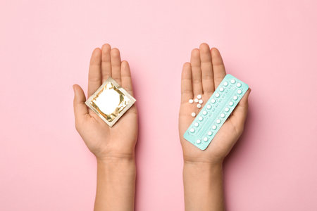 Woman holding condom and birth control pills on pink background, top view. safe sexの写真素材