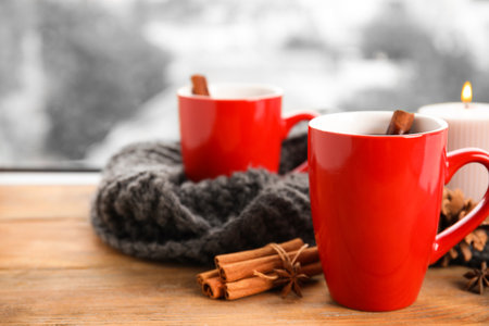 Cups of hot winter drink with scarf on window sill indoorsの写真素材