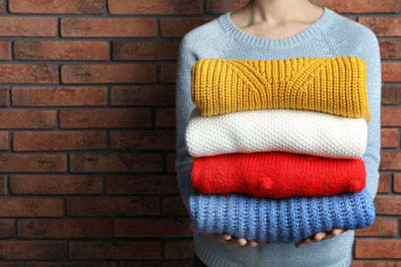 Woman holding pile of winter sweaters near brick wall, closeup view. Space for textの写真素材