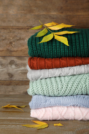 Stack of warm knitted clothes and autumn leaves on wooden background
