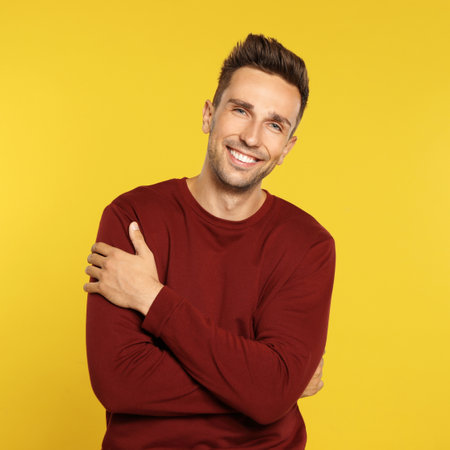 Happy young man in sweatshirt on yellow background. winter season