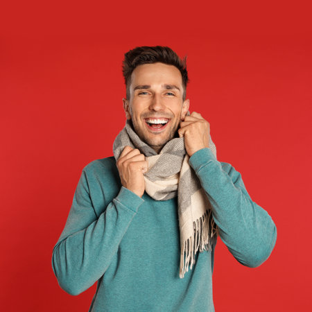 Happy young man in scarf and sweatshirt on red background. winter seasonの写真素材