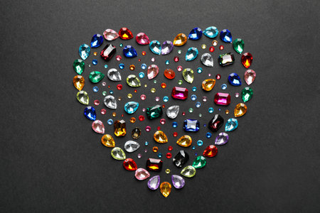 Heart shaped pile of different beautiful gemstones on black background, flat layの写真素材