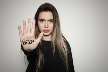 Young woman with the word HELP written on her palm against light background, focus on hand. Space...