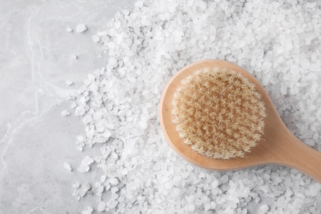 White sea salt for spa scrubbing procedure and brush on gray marble table, top viewの写真素材