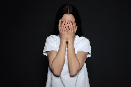 Upset young woman crying against dark backgroundの写真素材