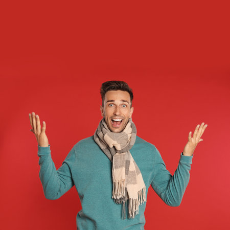 Excited young man in scarf and sweatshirt on red background. winter seasonの写真素材