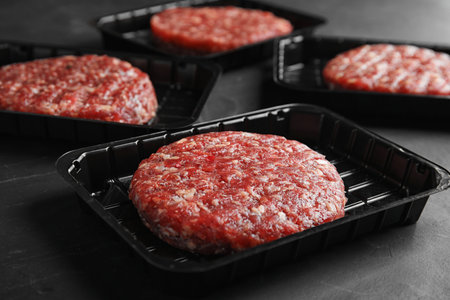 Plastic containers with raw meat cutlets for burger on gray table, closeupの写真素材