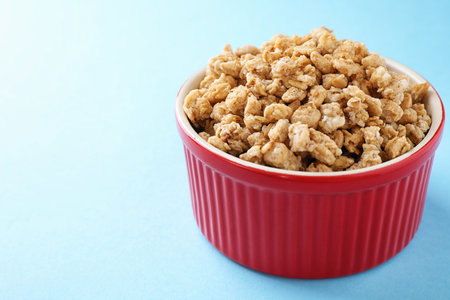 Bowl with healthy granola on light blue background. Space for text