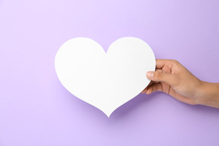 Woman holding blank paper heart on violet background, closeup. Space for textの写真素材