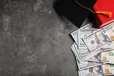 Flat lay composition with dollars and student graduation hat on stone background, space for text. Tuition fees conceptの写真素材