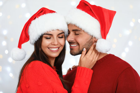 Lovely young couple in Santa hats against blurred festive lights. christmas celebrationの写真素材