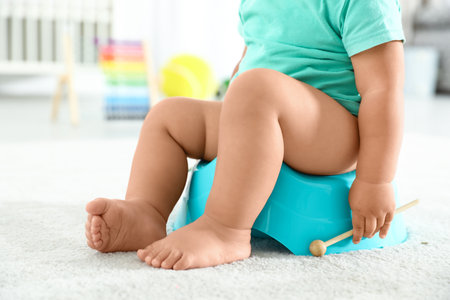 Little boy with wooden stick sitting on potty at home, closeupの写真素材