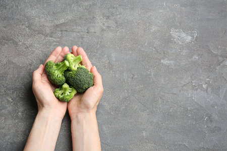 Female holding fresh green broccoli on gray stone table, top view. Space for textの写真素材