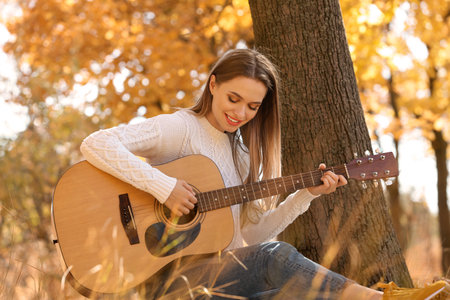 Teen girl playing guitar in autumn parkの写真素材