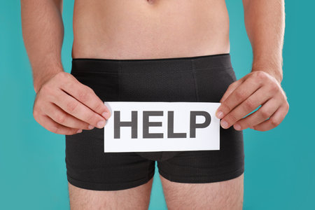 Man holding paper with word HELP on turquoise background, closeup. Urology problemsの写真素材