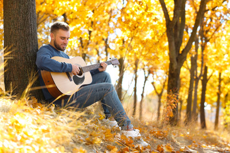 Young man playing guitar in autumn parkの写真素材