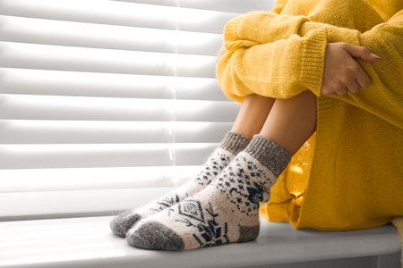Woman wearing knitted socks on window sill indoors, closeup. warm clothes