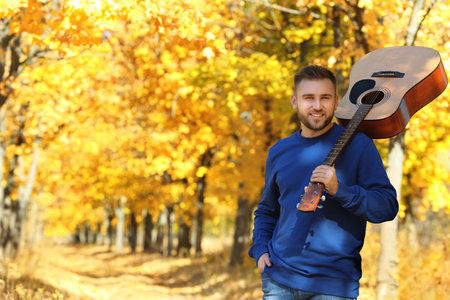 Young man with acoustic guitar in autumn parkの写真素材