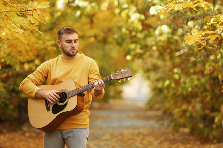 Young man playing guitar in autumn parkの写真素材