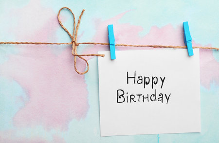 Card with words HAPPY BIRTHDAY hanging on clothesline, color backgroundの写真素材