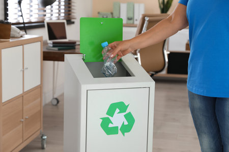 Woman throwing plastic bottle into recycling bin at office, closeupの写真素材