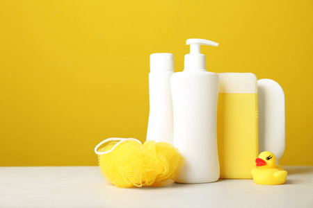 Baby cosmetic products, toy and accessories on white table against yellow background. Space for textの写真素材