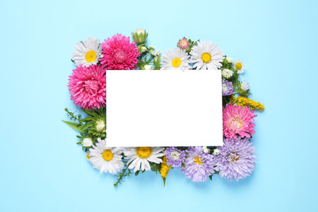 Flat lay composition with beautiful aster flowers and blank card on light blue background. Space for textの写真素材