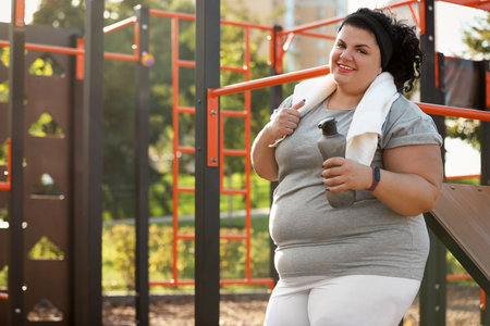 Beautiful overweight woman with towel and bottle on sports groundの写真素材