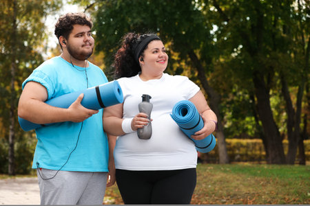 Overweight couple wearing sportswear with mats in parkの写真素材