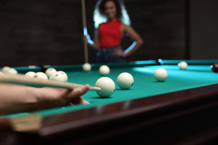 Young man playing billiard and blurred African-American woman on background, closeupの写真素材
